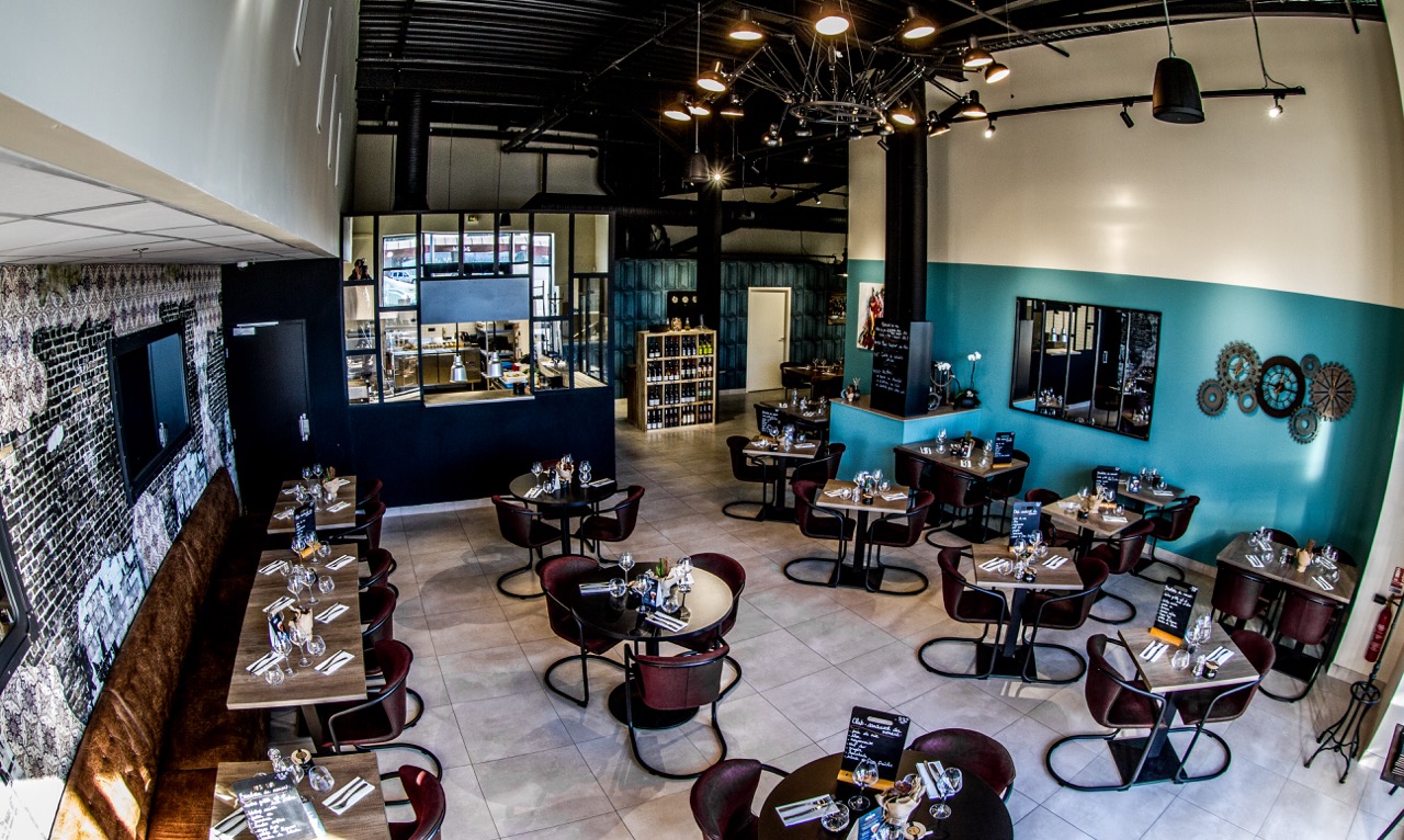 Salle du restaurant La Pôse Bistrot à Aigues-Mortes — tables dressées pour le déjeuner, cuisine ouverte sur la salle, mur brique